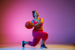 Young caucasian plus size female model's doing exercises on gradient purple background in neon light. Training in lunges with the ball. Concept of sport, healthy lifestyle, body positive, equality.