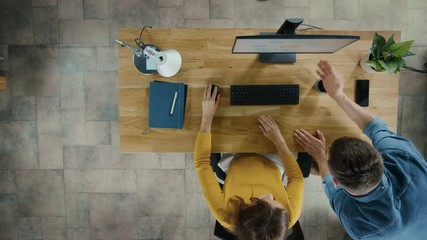 Wall Mural - Top View Camera Shot: Female Office Worker Uses Desktop Computer, Project Manager Stands Beside and gives Advice on Optimizing Workflow for Customer Experience Management. Gradually Unfocusing Picture