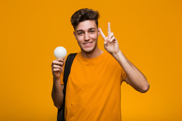 Young student man holding a light bulb looking sideways with doubtful and skeptical expression.