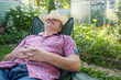 © RealPeopleStudio - Senior hispanic man in hat sitting leaning back on chair sleeping in outdoor summer flower garden