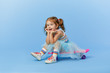 © oes - Cool little toddler girl in bright clothes sits on a skateboard and looking at the camera isolated on blue background