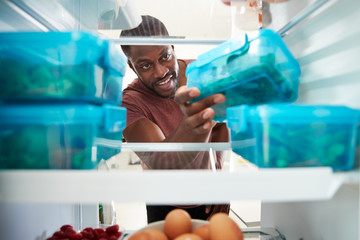 view looking out from inside of refrigerator as man takes out healthy packed lunch in container