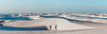 Travel Couple Trek Across Giant Sand Dunes With Lagoons In Lencois Maranhenses, One Of The Most Stunning Tourist Attractions In North-East Brazil