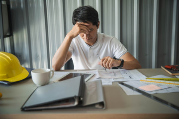 Feeling exhausted. Young architect massaging his nose and keeping eyes closed while sitting at his working place in office.