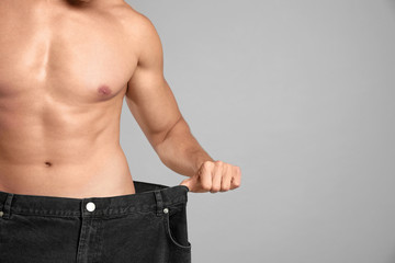 Wall Mural - Young man with slim body in old big size jeans on grey background, closeup view. Space for text