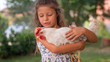 © Kitreel - Authentic moment of happy little smiling girl is holding a white hen outside the countryside house in a sunny summer day.