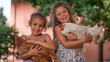© Kitreel - Authentic moment of two happy little smiling girls sisters are holding their hens outside the countryside house in a sunny summer day.