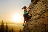 Beautiful Woman Climbing on the Rock at Foggy Sunset in the Mountains. Adventure and Extreme Sport Concept