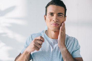 handsome young man holding toothbrush while having toothpain