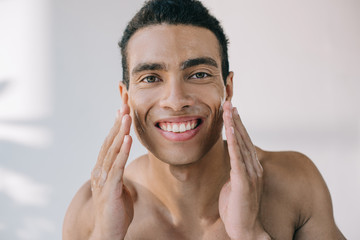 handsome young man with wet face touching it with hands while smiling and looking at camera