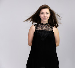 A portrait above the knee of a pretty beautiful fashionable adult brunette girl in a black dress on a white background. Standing right in front of the camera, showing different poses and emotions.