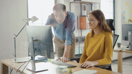 Wall Mural - Female Specialist Works on Desktop Computer, Project Manager Stands Beside and gives Advice on Optimizing Workflow for Customer Experience Management. Modern Office with Diverse Team of Professionals