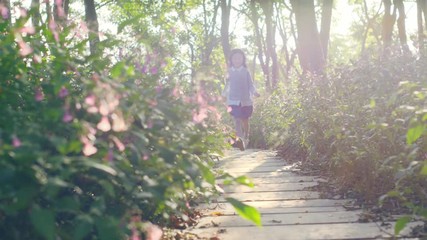 Wall Mural - 8 year-old beautiful little asian girl running on flagstone path through flower blossoms in park