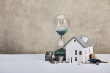 house model on white table with hourglass, coins and keys, real estate concept