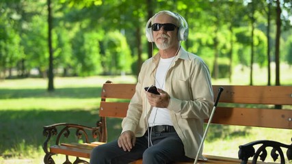 blind old man wearing earphones listening audiobook, voice message in cellphone
