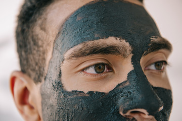 close up view of handsome young man with grey clay mask on face looking away