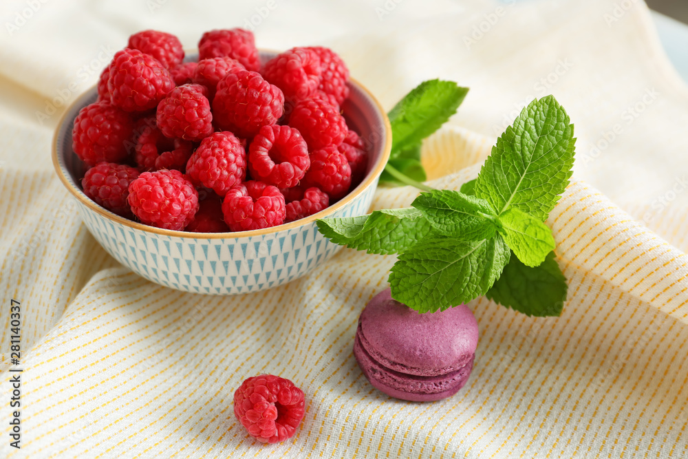 Bowl with fresh raspberries, macaron and mint on table