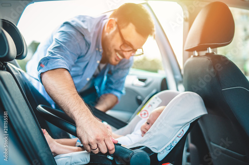 Fotomural Young father putting his baby boy on a safety child car seat.
