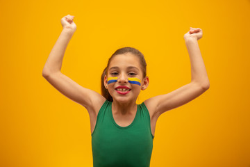 Football supporter, Brazil team. World Cup. Beautiful little girl cheering for her team on yellow background