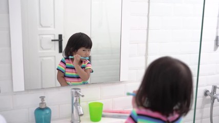 Wall Mural - toddler independently brush her own teeth in the bathroom looking at the mirror