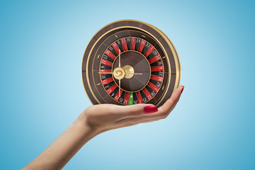 Poster - Side closeup of woman's hand facing up and holding small casino wheel on light blue gradient background.