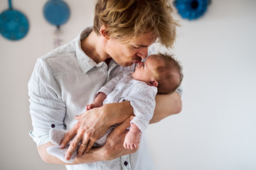 a young father holding a newborn baby at home, kissing.
