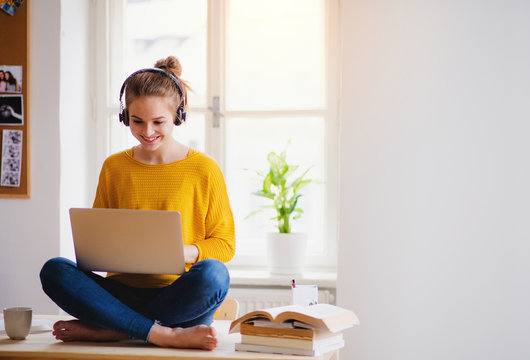 A young female student sitting at the table, using headphones when studying.