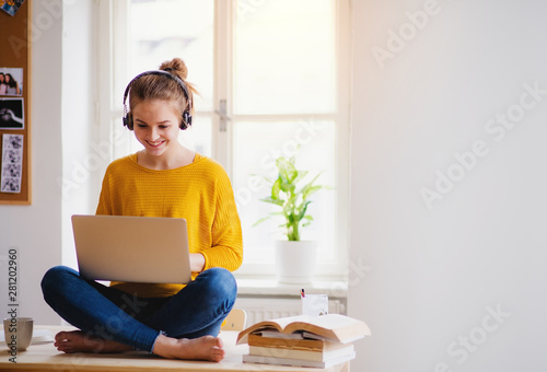Cuadros en Lienzo A young female student sitting at the table, using headphones when studying