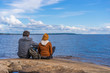 © Tatyana_Andreyeva - Tourists man and woman sitting on northern lake shore in summer day. People relaxing and admiring beautiful landscape. Travelling and discovering distant places of Earth. Onega lake, Karelia, Russia