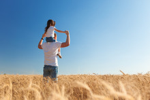 Happy Father And Daughter Walk In The Summer Field. Nature Beauty, Blue Sky And Field With Golden Wheat. Outdoor Lifestyle. Freedom Concept.