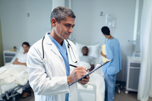 Male Doctor Writing On Clipboard In The Ward At Hospital