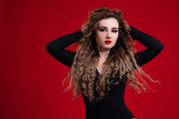 Young woman with her hands behind her head, red lips and curly hair posing. Beautiful woman with clean fresh skin and healthy curly hair. Sexy young woman with perfect make up. Afro curls hair.