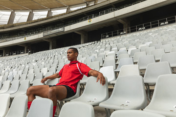 Wall Mural - Thoughtful African American male rugby player sitting alone in stadium