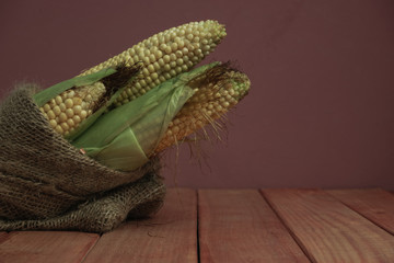 Poster - Fresh Sweet corn in bag on a red   wooden table and beautiful red wall background.