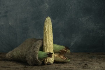 Poster - Fresh Sweet corn in bag on a old oak  wooden table and beautiful grey wall background.