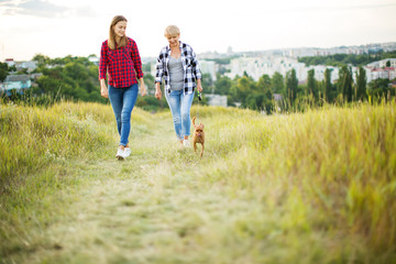 Mother and adult daughter with dog outdoor in park.