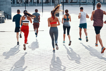 Full length rear view of people in sports clothing jogging while exercising on the sidewalk outdoors