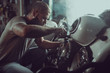 Handsome bearded man repairing his motorcycle in the garage. A man wearing jeans and a t-shirt