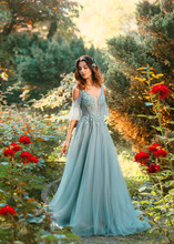 Affectionate Bride In Light Blue Dress In Green Garden With Red Lush Roses, Princess With Dark Hair Looks Down, Pretty Model Poses For Charming Photo With Creative Colors, Symbol Of Passing Summer