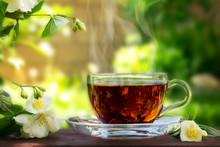 Glass Cup With Tea And Jasmine Twig On Wooden Table, On Blurred Background