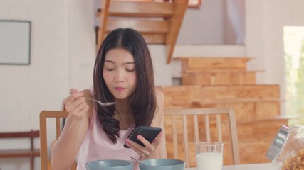 Wall Mural - Asian Lesbian lgbtq women couple have breakfast at home, Young Asia lover girls happy using mobile phone check news while drink juice, cornflakes cereal and milk in kitchen in the morning concept.