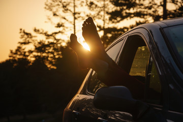 Barefooted young woman in the car against sunset