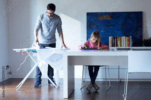 Fotomural Pretty little girl drawing on notebook while her father ironing a shirt at home