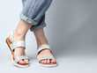 Fragment of female legs in blue jeans and trendy leather sandals on white background. Women's stylish summer shoes. Minimalistic fashion shot