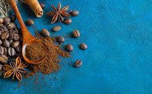 Coffee Grains Scattered On A Blue Textural Background, Anise Stars, Cinnamon Sticks And Ground Coffee In A Wooden Spoon. Top View