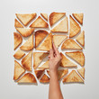 © Yaroslav Danylchenko/Stocksy - The hand of the girl makes a pattern of square-shaped pieces of fried toast on a gray background. Flat lay