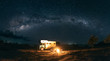 © Akela - from alp to alp/Stocksy - panorama shot of a family sitting at a bonfire under the milky way with a camping truck