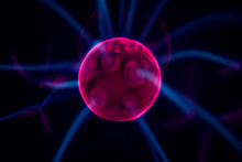Detail View Of An Electric Plasma Ball With Red Center In Focus And Multiple Blue Rays Moving Around Against Pitch Black Background