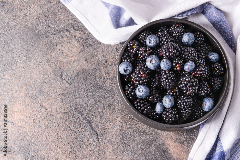 Bowl with tasty blackberries and blueberries on grey table