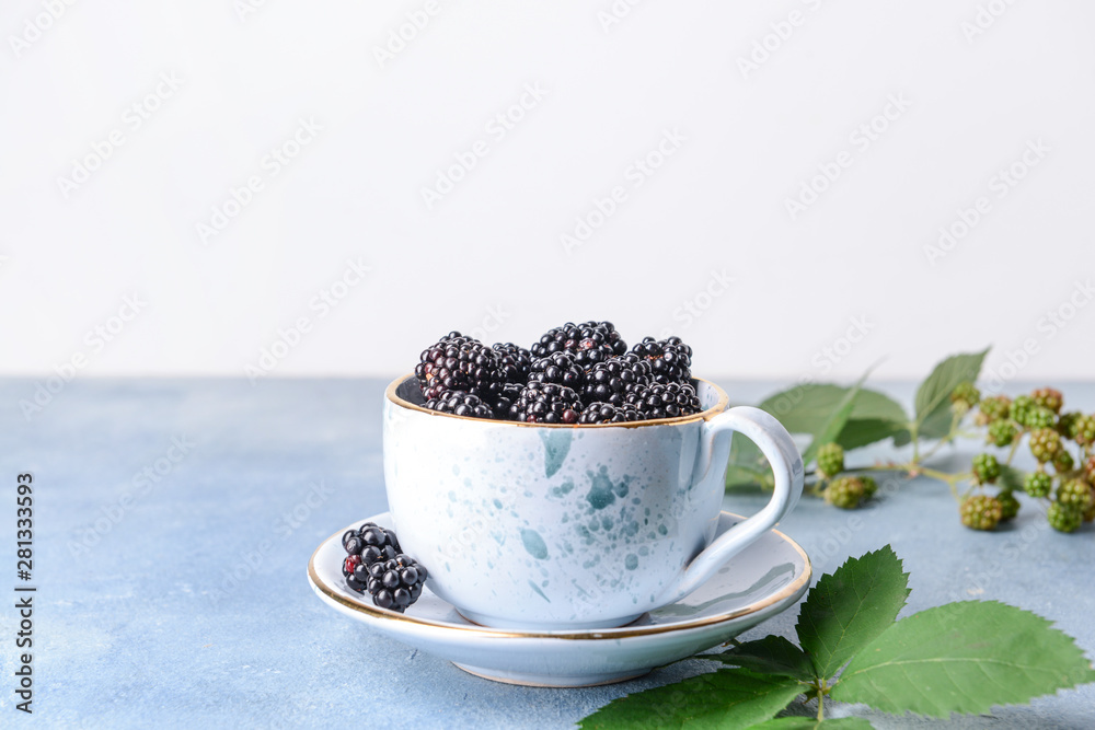 Cup with tasty blackberries on color table